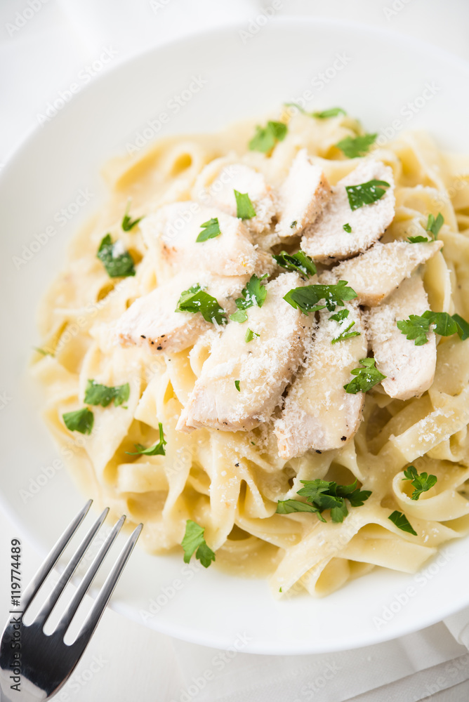 Pasta fettuccine alfredo with chicken, parmesan and parsley on white background close up. Italian cuisine.