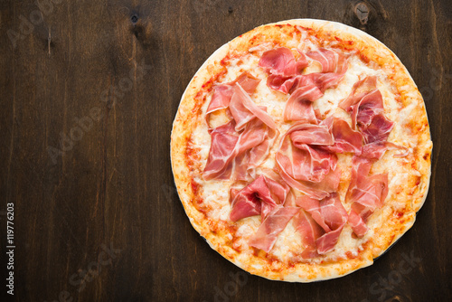 Foto Pizza with prosciutto (parma ham) on dark wooden background top view