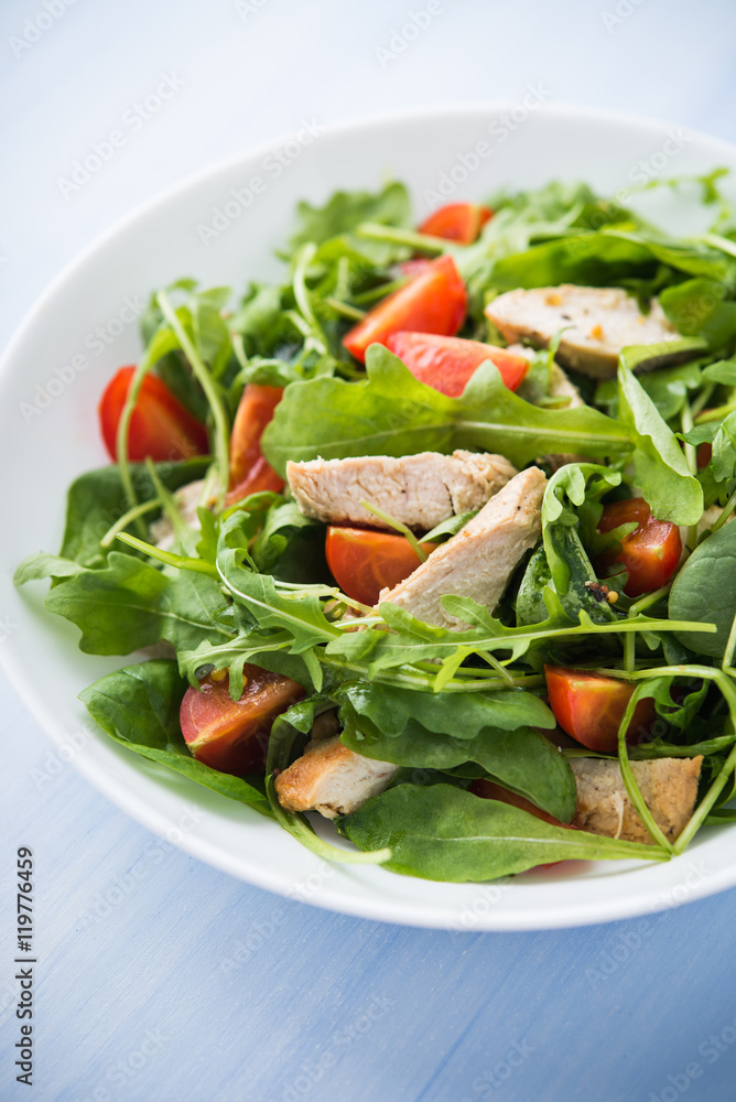 Fresh salad with chicken, tomato and greens (spinach, arugula) on blue wooden background close up. Healthy food.