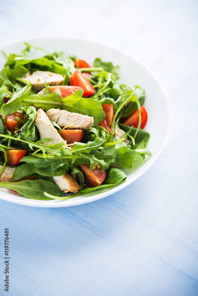 Fresh salad with chicken, tomato and greens (spinach, arugula) on blue wooden background close up. Healthy food.