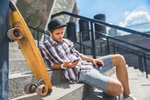 Thoughtful male skater listening to music form earphones