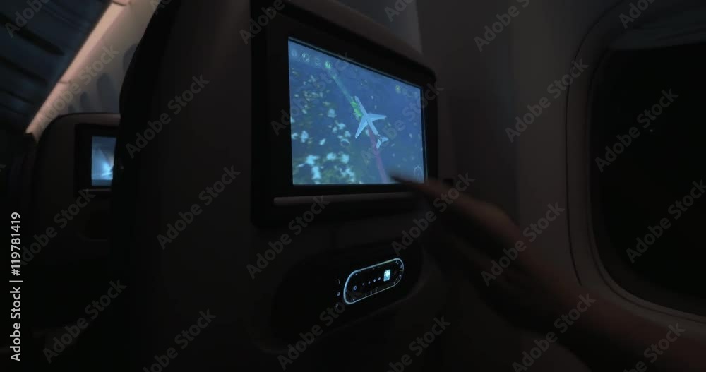 Woman using touchscreen seat monitor to look at flight path during night travel by plane Woman using touchscreen seat monitor to look at flight path during night travel by plane