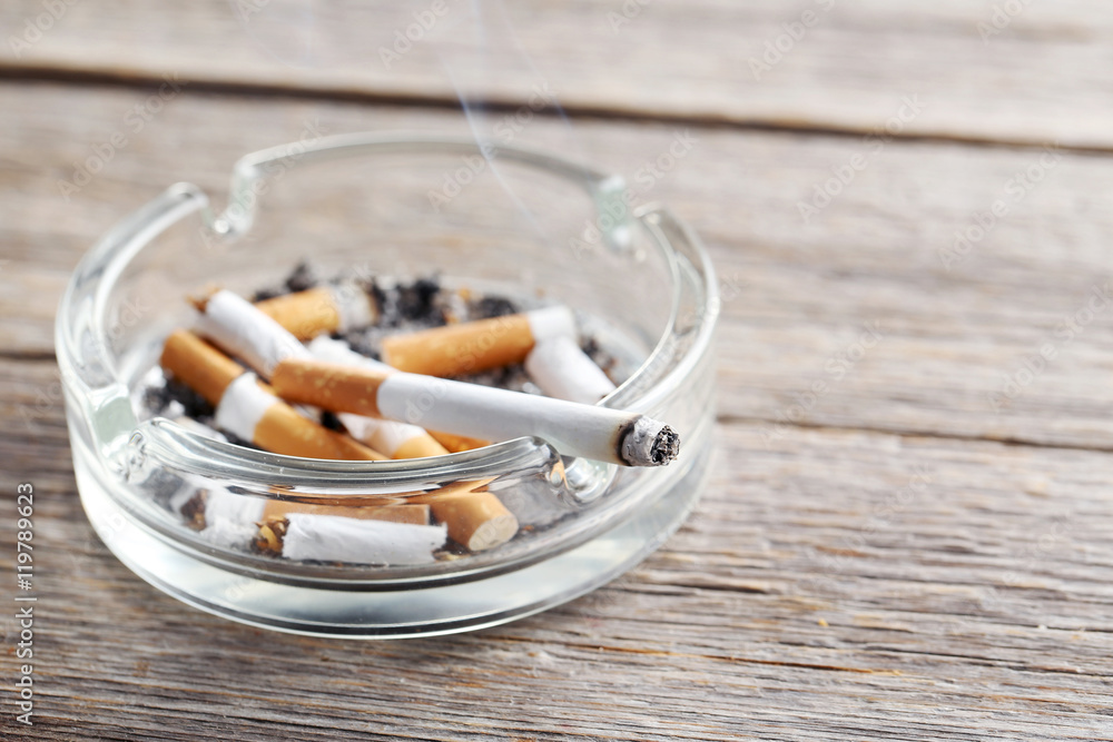 Cigarette butts with ash in ashtray on grey wooden table Cigarette butts with ash in ashtray on grey wooden table
