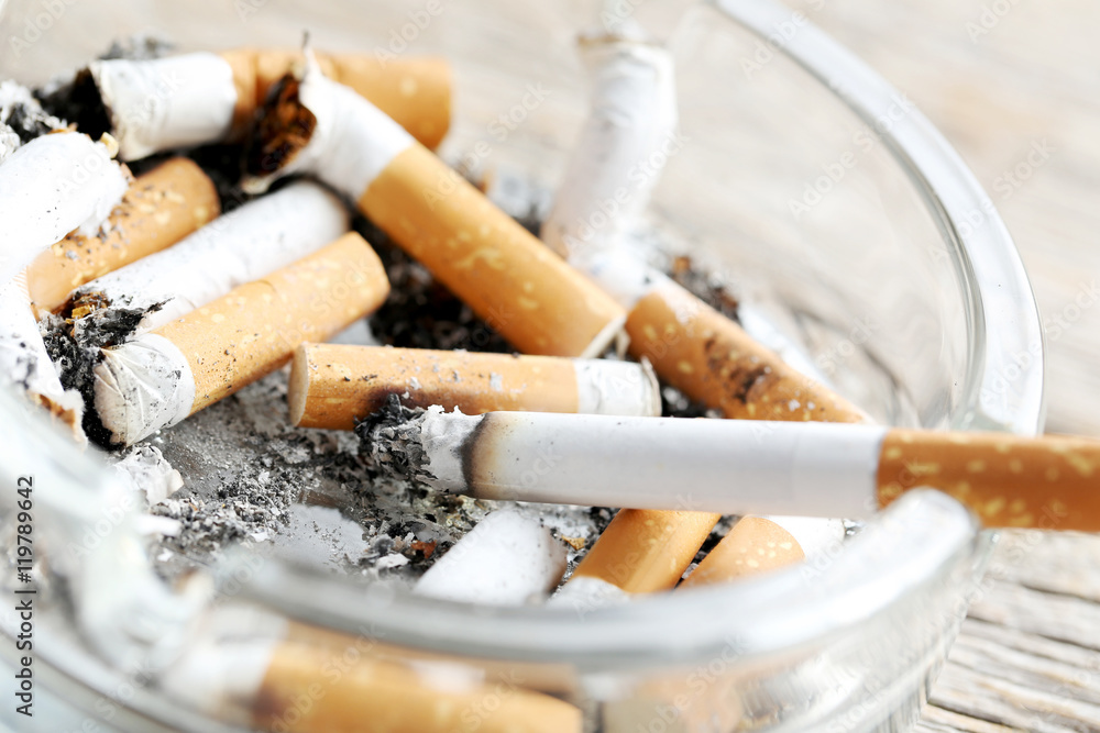 Cigarette butts with ash in ashtray on grey wooden table Cigarette butts with ash in ashtray on grey wooden table