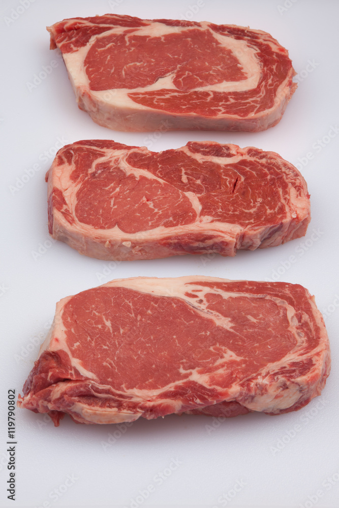 Three Ribeye steaks on a white cutting board
