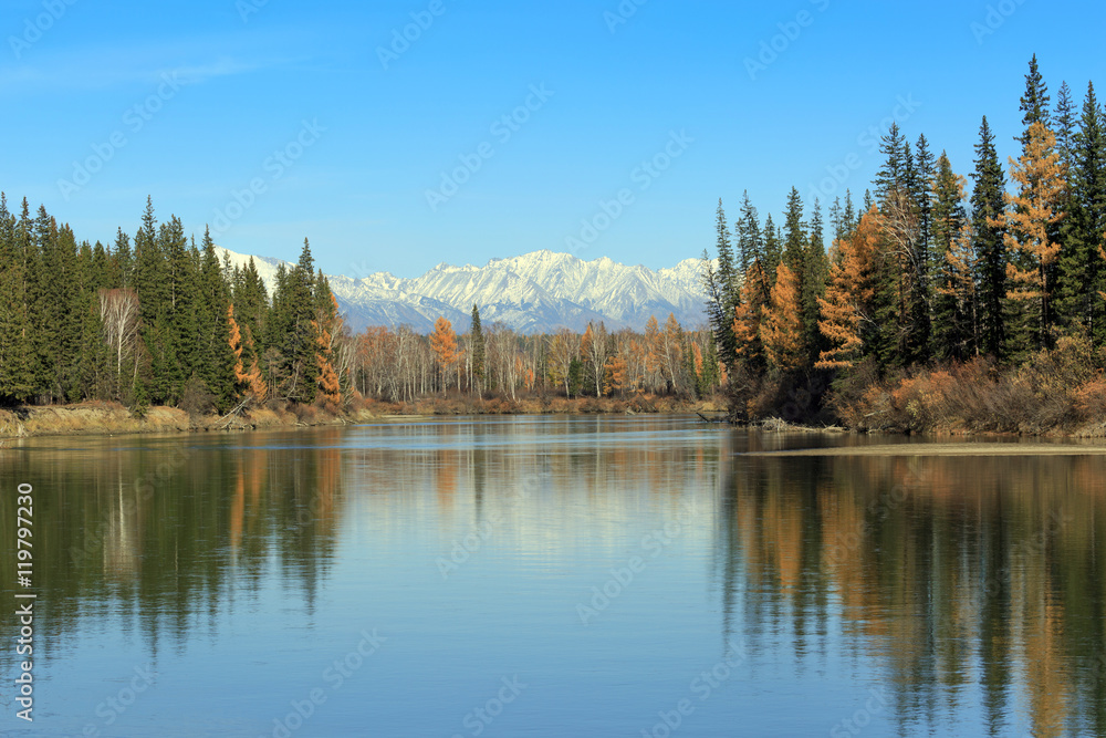 Bright autumn landscape, trees, and mountains reflected in the river.