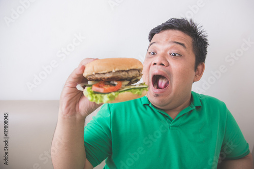 Overweight man eating hamburger at home