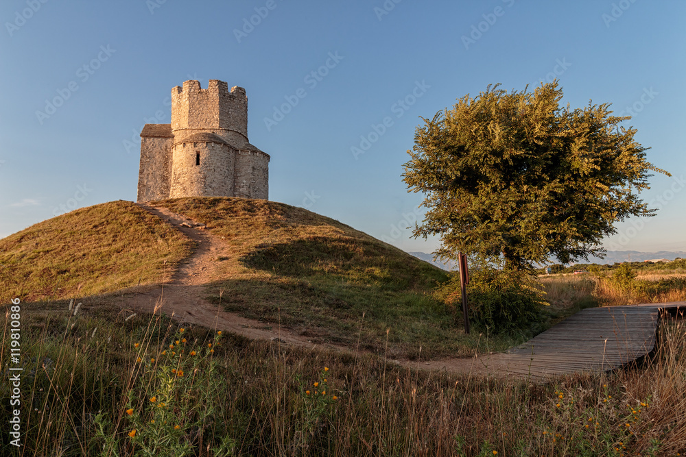 Old small stone church of St. Nicholas on hill near city of  Nin in Croatia. Golden hour.