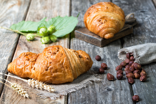 Fresh croissants, spikelets and hazelnuts on wooden background