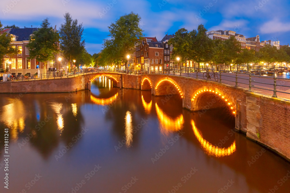 Amsterdam canal, bridge and typical houses, boats and bicycles during evening twilight blue hour, Holland, Netherlands.
