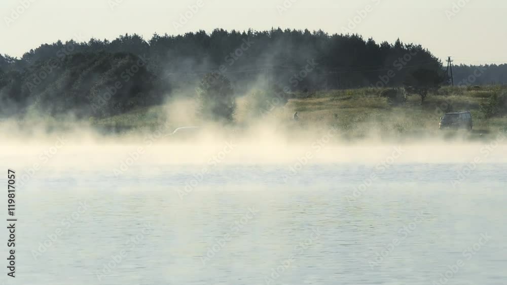 Scenic landscape with fog rising over a lake or river at dawn in summer with tall green trees on background Scenic landscape with fog rising over a lake or river at dawn in summer with tall green trees on background