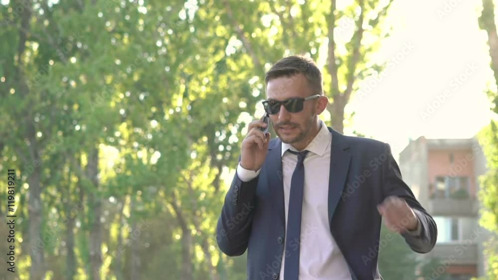 Angry man in black speaking on phone, undressing sunglasses and is nervous Angry man in black speaking on phone, undressing sunglasses and is nervous