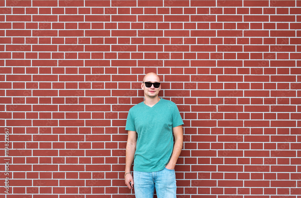 The bald man in sunglasses against the background of a red brick wall The bald man in sunglasses against the background of a red brick wall