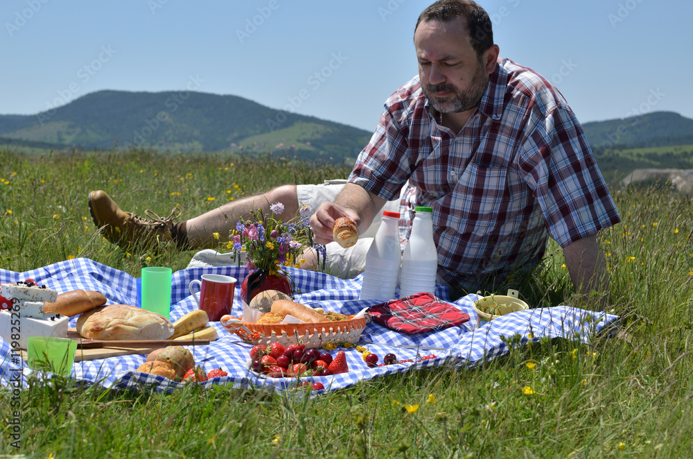 Obraz premium Man on picnic is taking a bun and preparing to eat it, on sunny day
