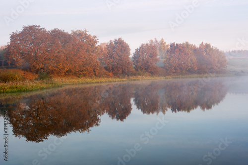 Foggy morning over the lake, fall trees reflected in water.
