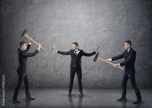 Fotografia Businessman separating two fighting businessmen with hammers