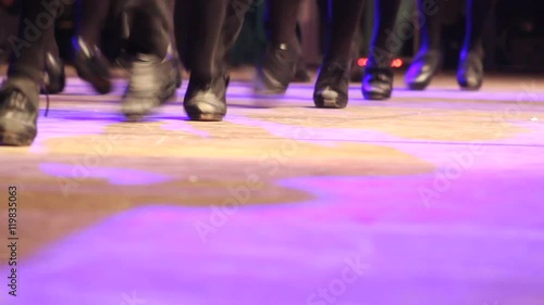 Two rows of people doing Irish dance with traditional step shoes. Close up double line of female dancing feet on stage became one. Music, tradition and culture of Ireland. Celtic show on wooden floor