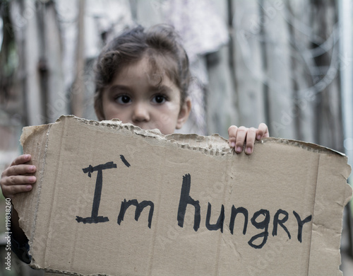 Little girl holding a sheet of cardboard. On the cardboard label "I am hungry." The child is three years.
