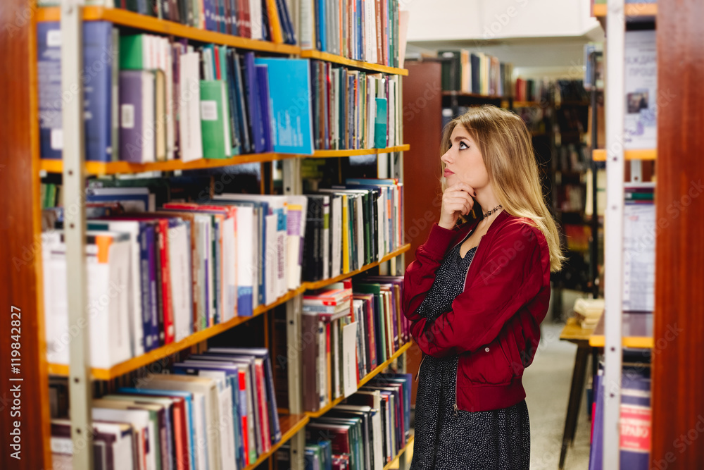 Pensive girl chosing a book in college library. Education concept Pensive girl chosing a book in college library. Education concept