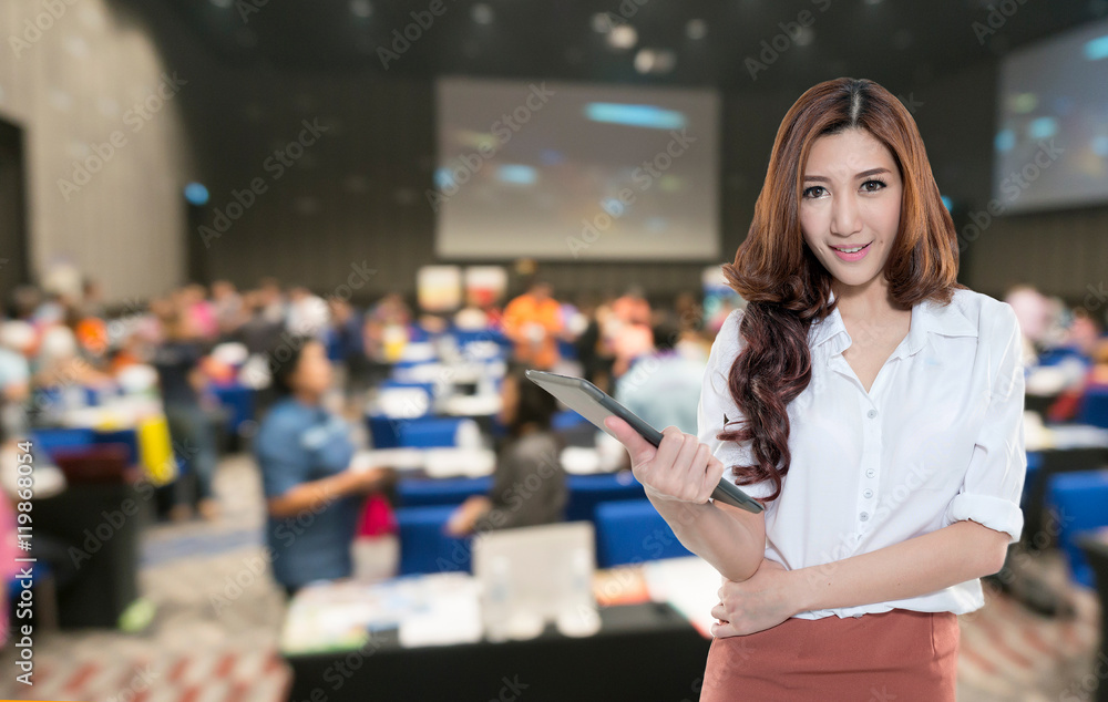 Beautiful asian woman holding document on the Abstract blurred photo of conference hall or seminar room with attendee background.