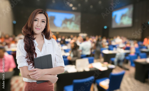 Beautiful asian working woman on the Abstract blurred photo of conference hall or seminar room with attendee background.