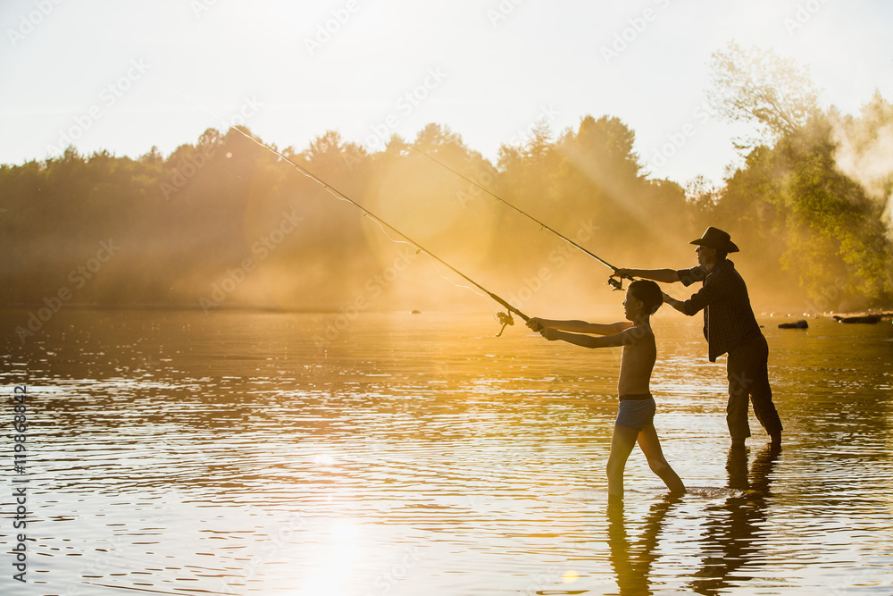 Fisherman in a cowboy hat with his son, sunset, fog. A man stands in the  water. Autumn fishing. Hobbies, outdoor recreation. Fishing on Spinning.  Silhouette. Stock Photo