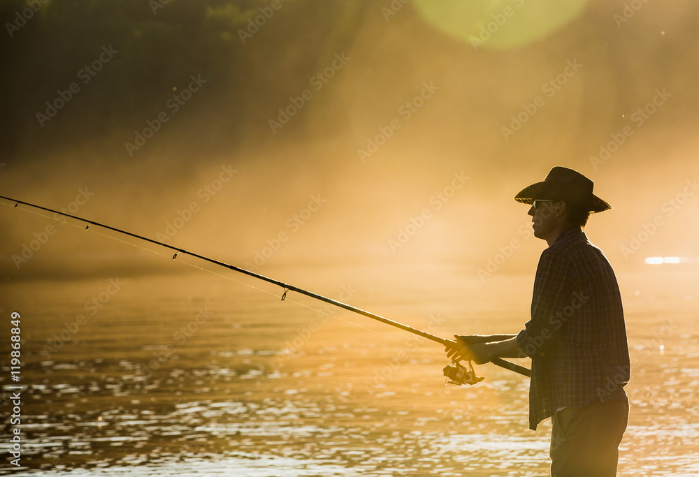 Fisherman in a cowboy hat sunset, fog. A man stands in the water. Autumn  fishing. Hobbies, outdoor recreation. Fishing on Spinning. Stock Photo