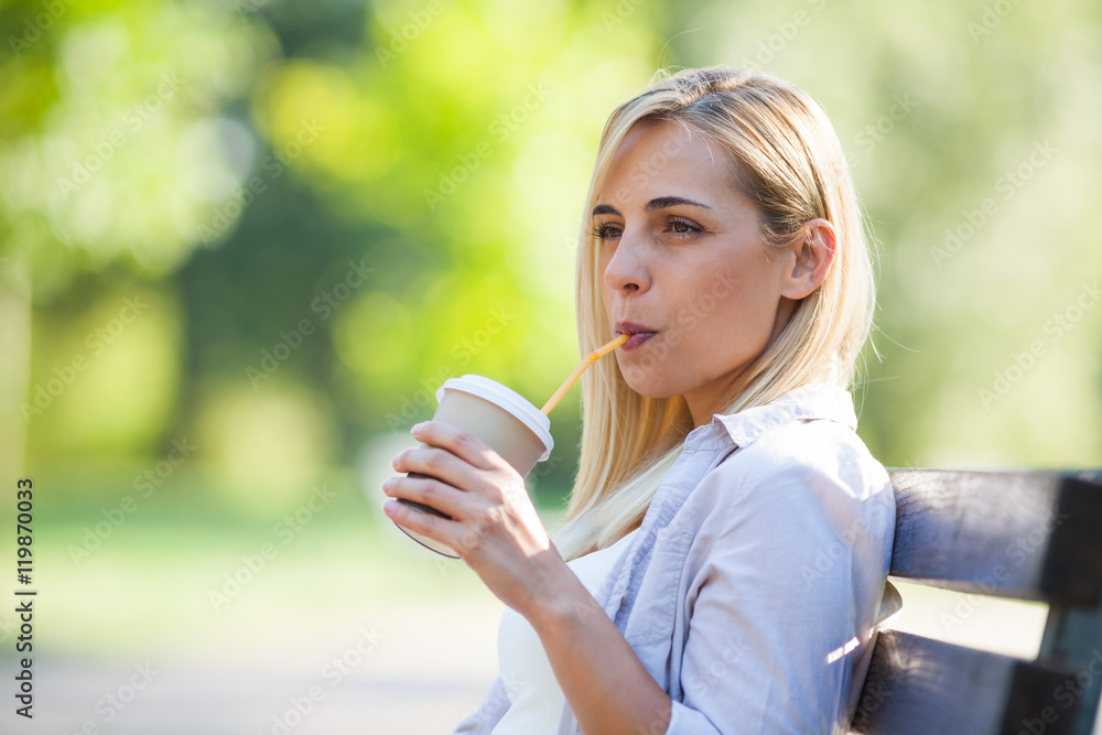 Young happy woman is drinking coffee to go in park.