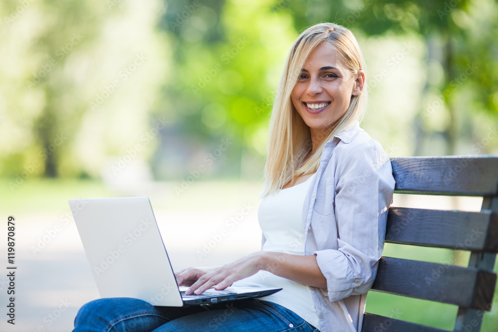 Young happy woman is sitting in park and using laptop. Young happy woman is sitting in park and using laptop.