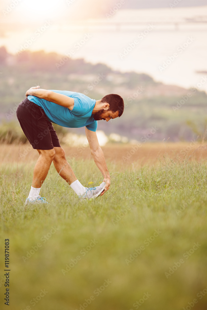 Athletic runner doing stretching exercise, preparing for running in the nature with the city in background. Healthy lifestyle Athletic runner doing stretching exercise, preparing for running in the nature with the city in background. Healthy lifestyle