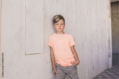 Trendy boy leaned on the wall and is confidently looking forward . He has cool hair . With one hand he put in his pocket . 