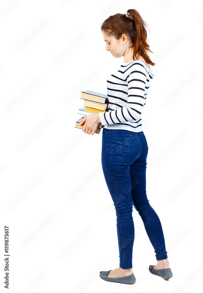 Girl carries a heavy pile of books. back view. Rear view people collection. Girl in a striped sweater standing sideways and holding a stack of textbooks. Girl carries a heavy pile of books. back view. Rear view people collection. Girl in a striped sweater standing sideways and holding a stack of textbooks.