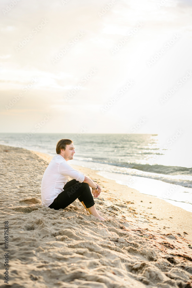 Handsome stylish groom posing on the beach