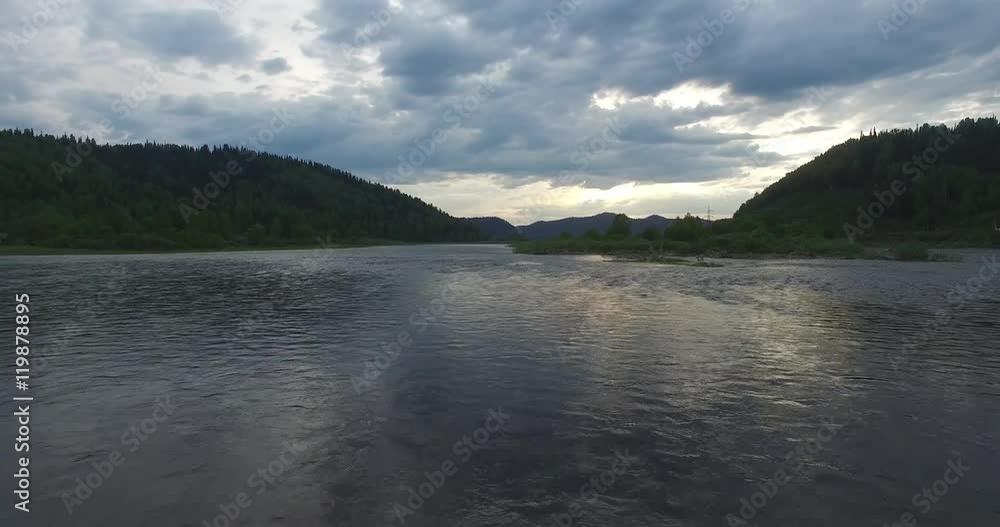 Cloudy sky is reflected in the surface of the river. / Low flying quadrocopters with the camera above the water edge