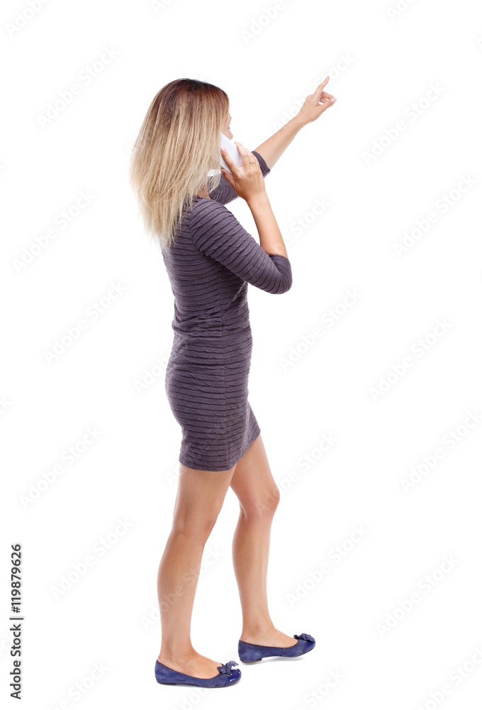 back view of pointing young beautiful woman and using a mobile phone. Isolated over white background. Blonde in violet short dress talking on the phone pointing up. back view of pointing young beautiful woman and using a mobile phone. Isolated over white background. Blonde in violet short dress talking on the phone pointing up.