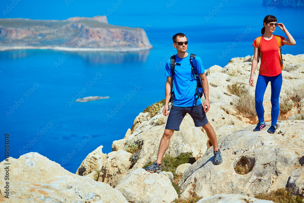 couple of travelers with backpack standing on the cliff against sea and blue sky at early morning