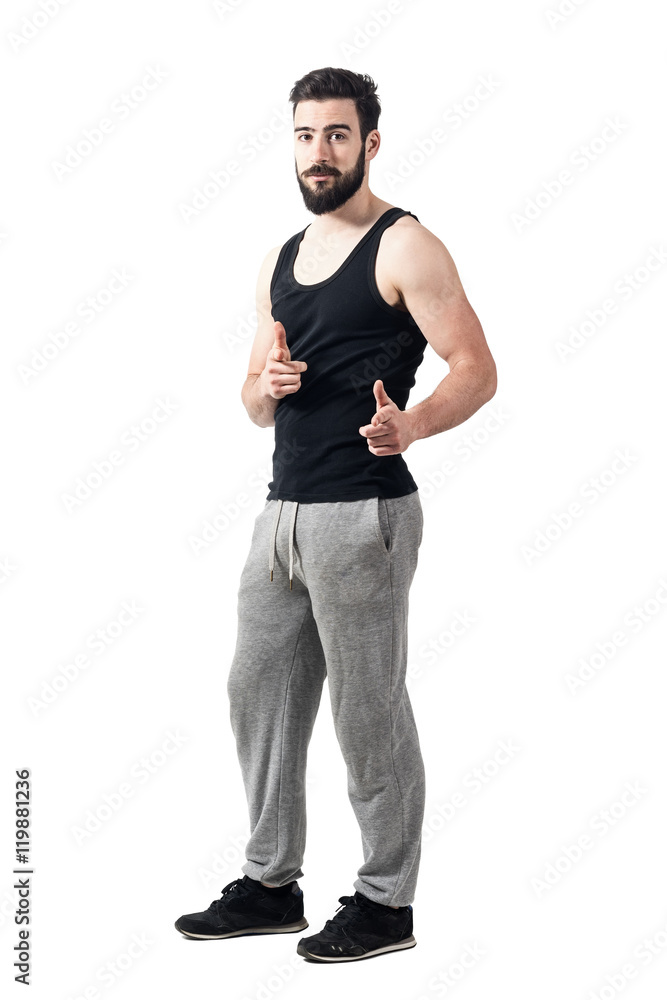 Young athlete in tank top pointing fingers at camera. Toned desaturated full body length portrait isolated on white studio background. Young athlete in tank top pointing fingers at camera. Toned desaturated full body length portrait isolated on white studio background.