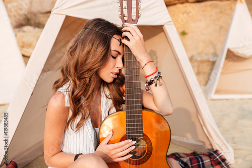 Thoughtful young woman with guitar in teepee on the beach © Drobot Dean