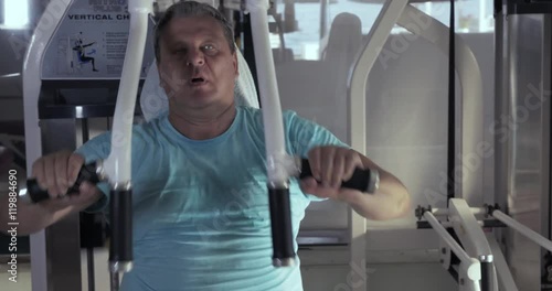 Close-up of grown man in gym sitting on the exerciser and performs exercises chest press and then resting