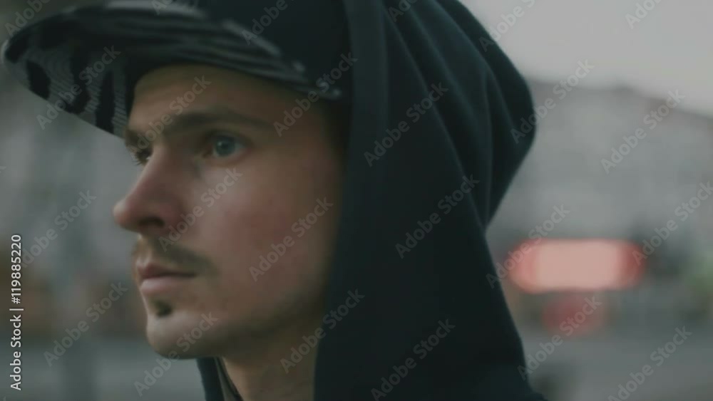 A young man in a cap and hood removes the headphone out of the ear A young man in a cap and hood removes the headphone out of the ear