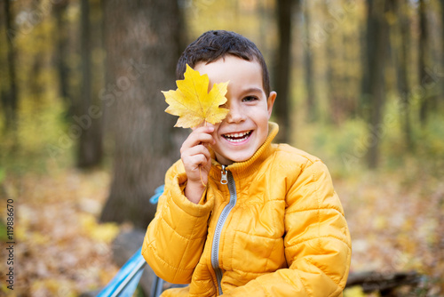 Cheerful boy smiling and hiding behind yellow leaf © Ksenia Kuznetsova