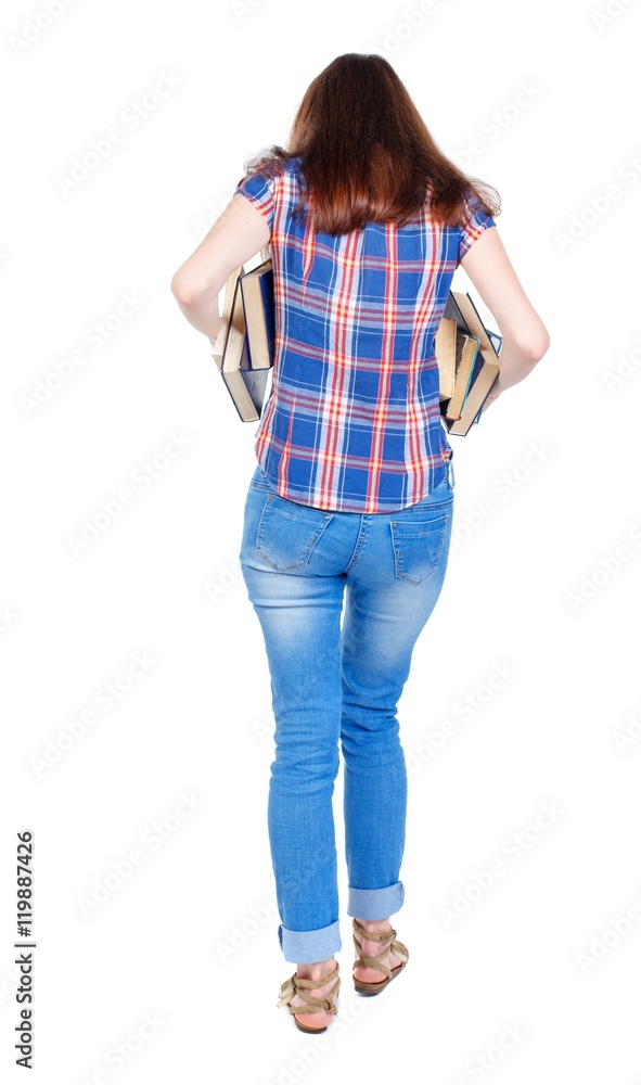Girl comes with stack of books. back side view. Girl in plaid shirt holding out underarm textbooks. Girl comes with stack of books. back side view. Girl in plaid shirt holding out underarm textbooks.