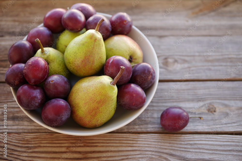 Ripe fresh pears and plums in a bowl on a wooden background close up. Autumn harvest of fruit. Ripe fresh pears and plums in a bowl on a wooden background close up. Autumn harvest of fruit.