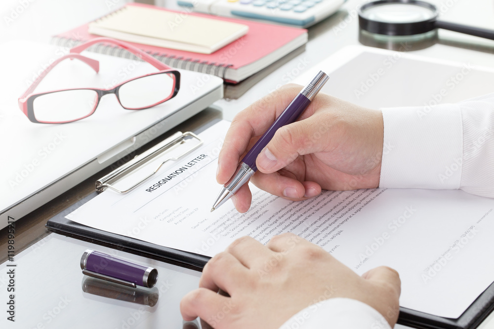 Businessman signing his resignation letter on his desk before sending to his boss to resign his job. Businessman signing his resignation letter on his desk before sending to his boss to resign his job.