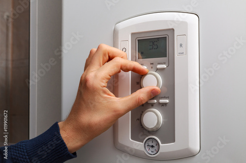 Men hand regulate low temperature on 35 degree in control panel of central heating.