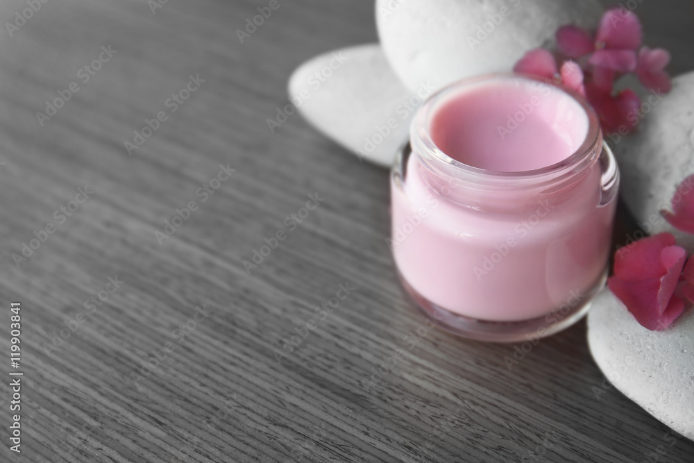 Facial cream with pink petals and pebbles on wooden background Facial cream with pink petals and pebbles on wooden background