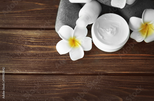 Facial cream with exotic flowers and pebbles on wooden background