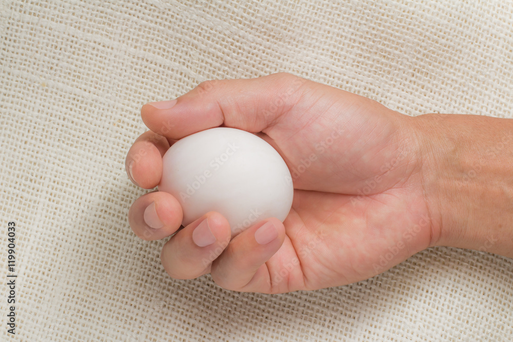 Hand holding white egg on sackcloth Hand holding white egg on sackcloth