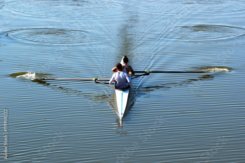 Team of two women rowers in a boat, sweeping on tranquil river