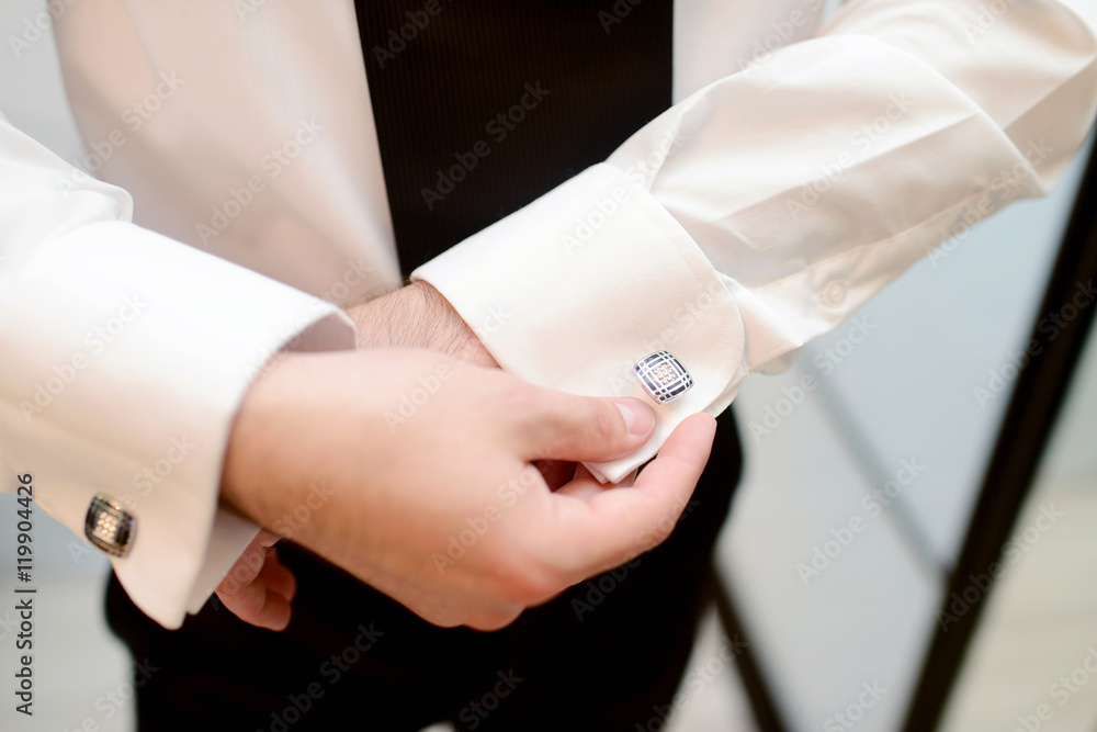 Groom is wearing cuff-links indoors. Male portrait of handsome guy. Beautiful model boy in colorful wedding clothes. Man is posing Groom is wearing cuff-links indoors. Male portrait of handsome guy. Beautiful model boy in colorful wedding clothes. Man is posing